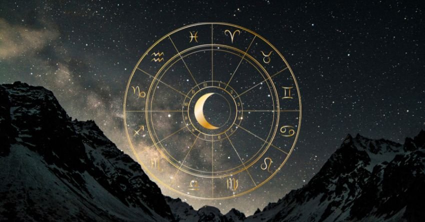 Golden zodiac wheel with a glowing crescent moon above dark mountain peaks and a dramatic cosmic sky